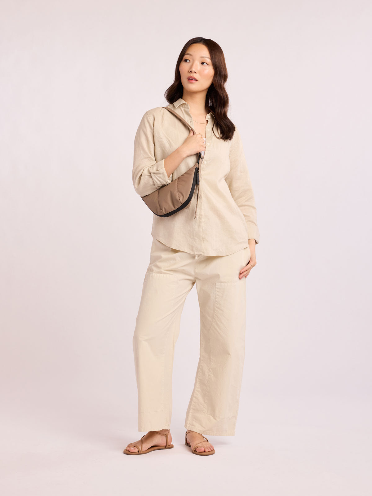 Model in beige outfit wearing CALPAK Luka Crescent Tote bag in light brown Chocolate with shoulder strap and bag is expandable up to 2"; CBL2601-CHOCOLATE