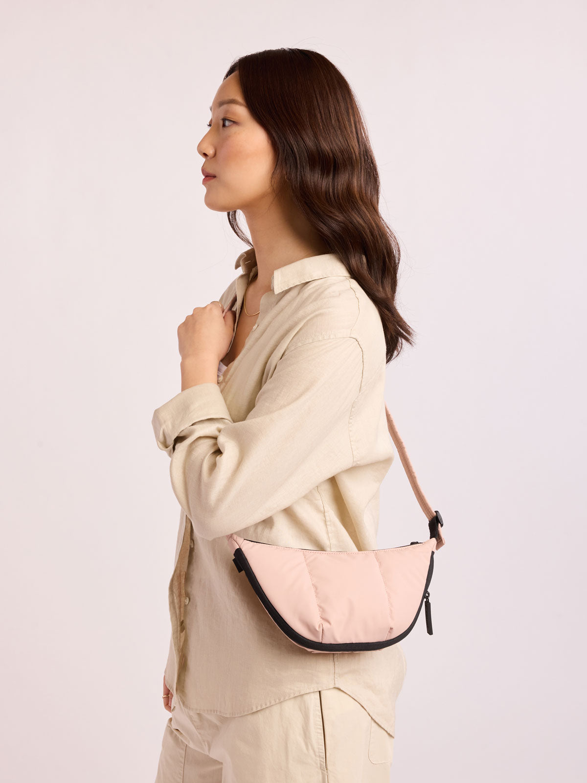 Model in beige outfit wearing CALPAK Luka Crescent Bag in light pink Rose Quartz; CBL2601-ROSE-QUARTZ