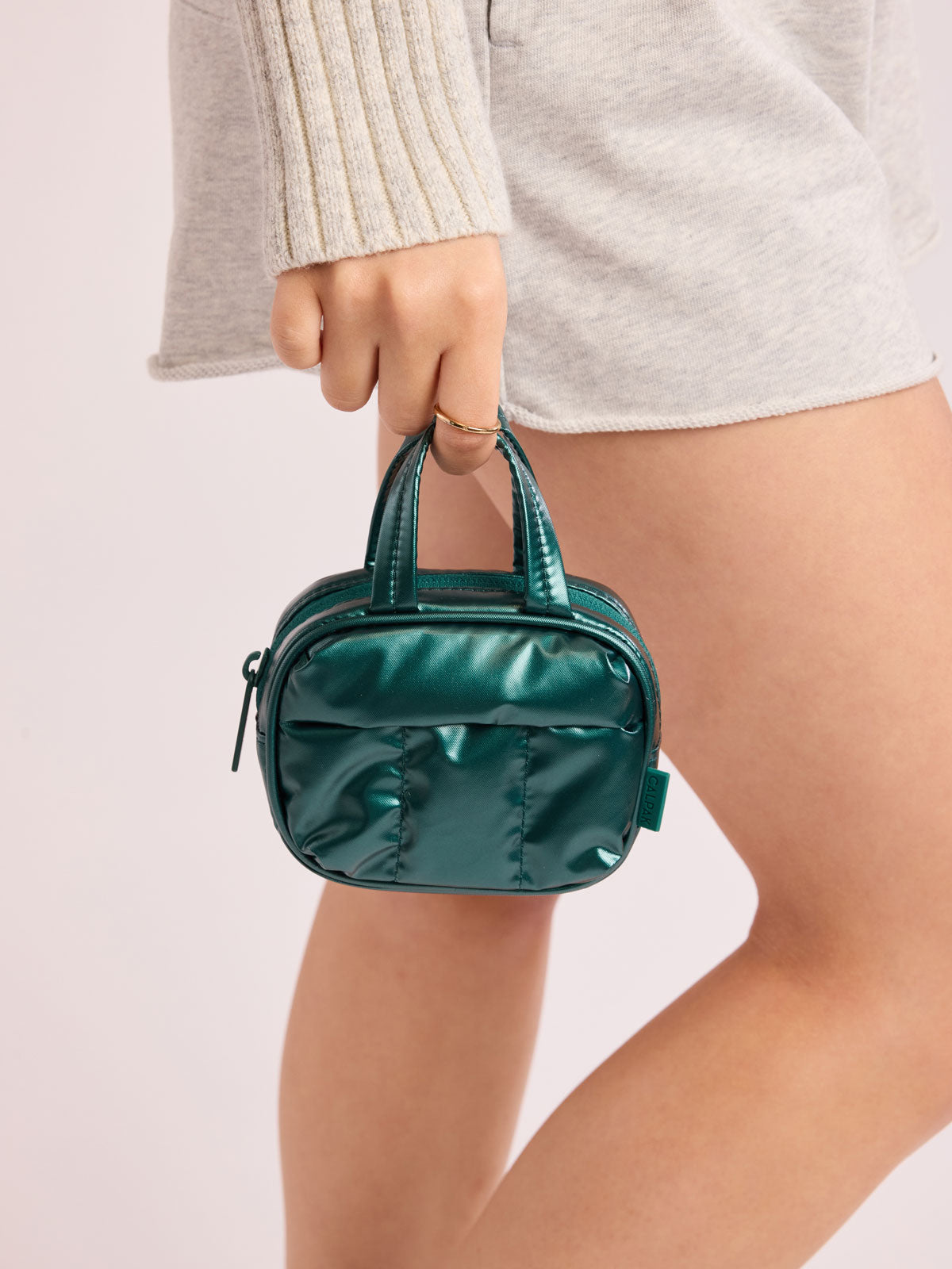 Model holding CALPAK Luka Duffel Zip Bag Charm in dark green shiny Glazed Kale ; ALK2501-GLAZED-KALE