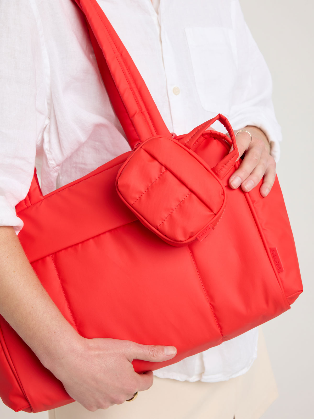 Person with CALPAK Luka Duffel Zip Bag Charm in red Tomato; ALK2501-TOMATO