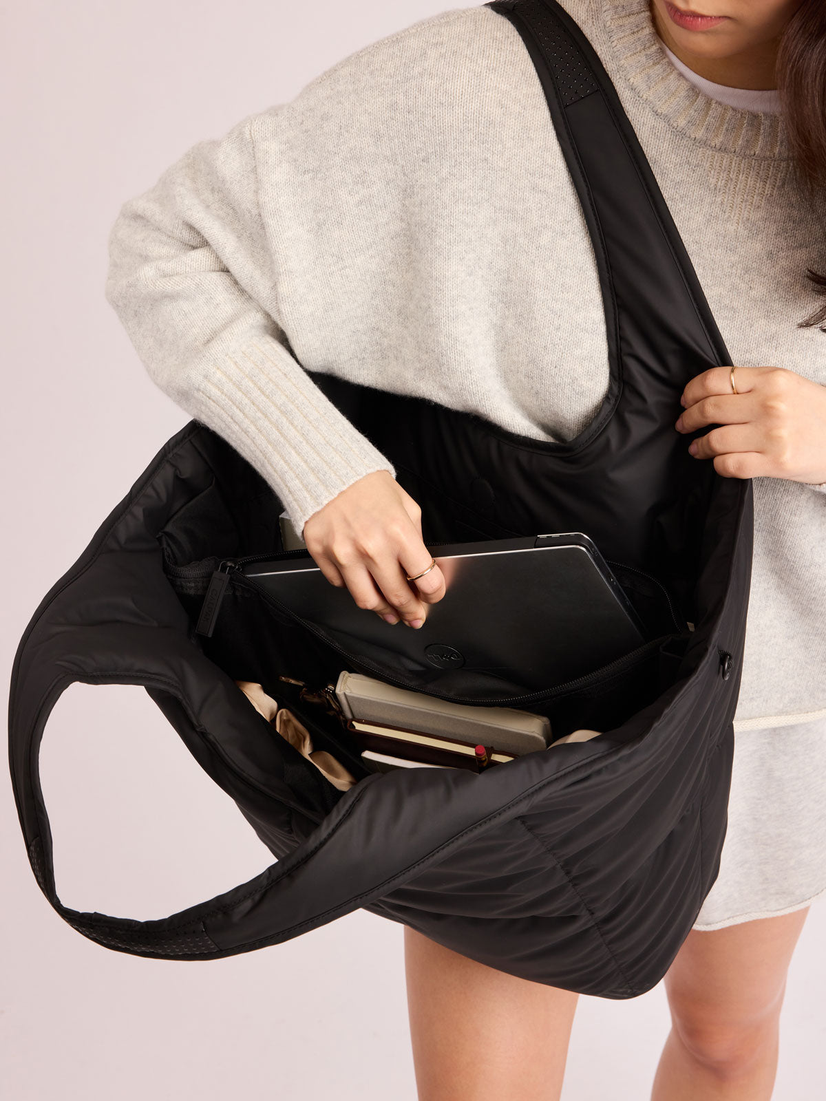 Model adding laptop into the CALPAK Luka Everything Tote in black; AET2601-MATTE-BLACK