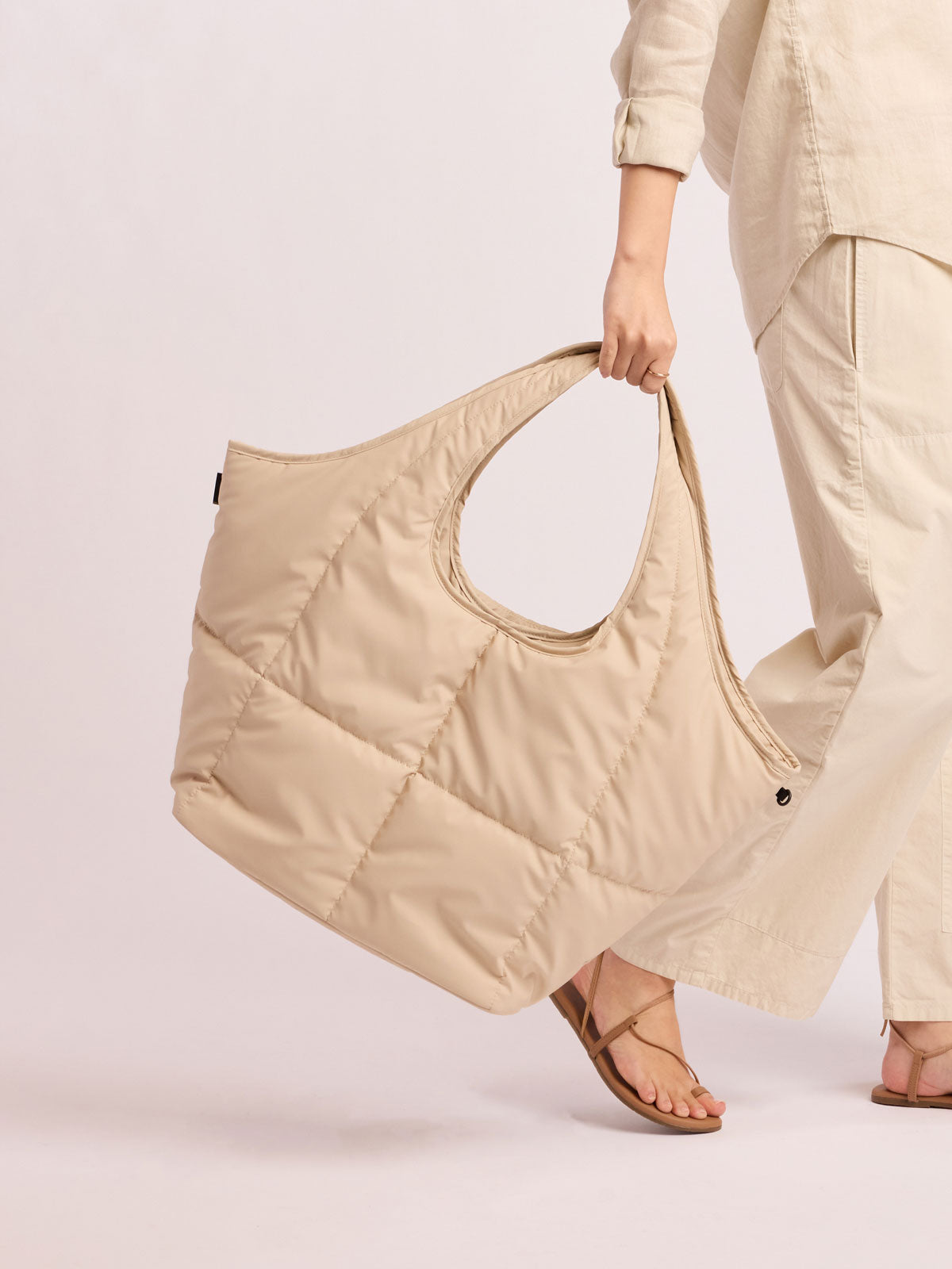 Model holding the CALPAK Luka Everything Tote in off-white beige Oatmeal; AET2601-OATMEAL
