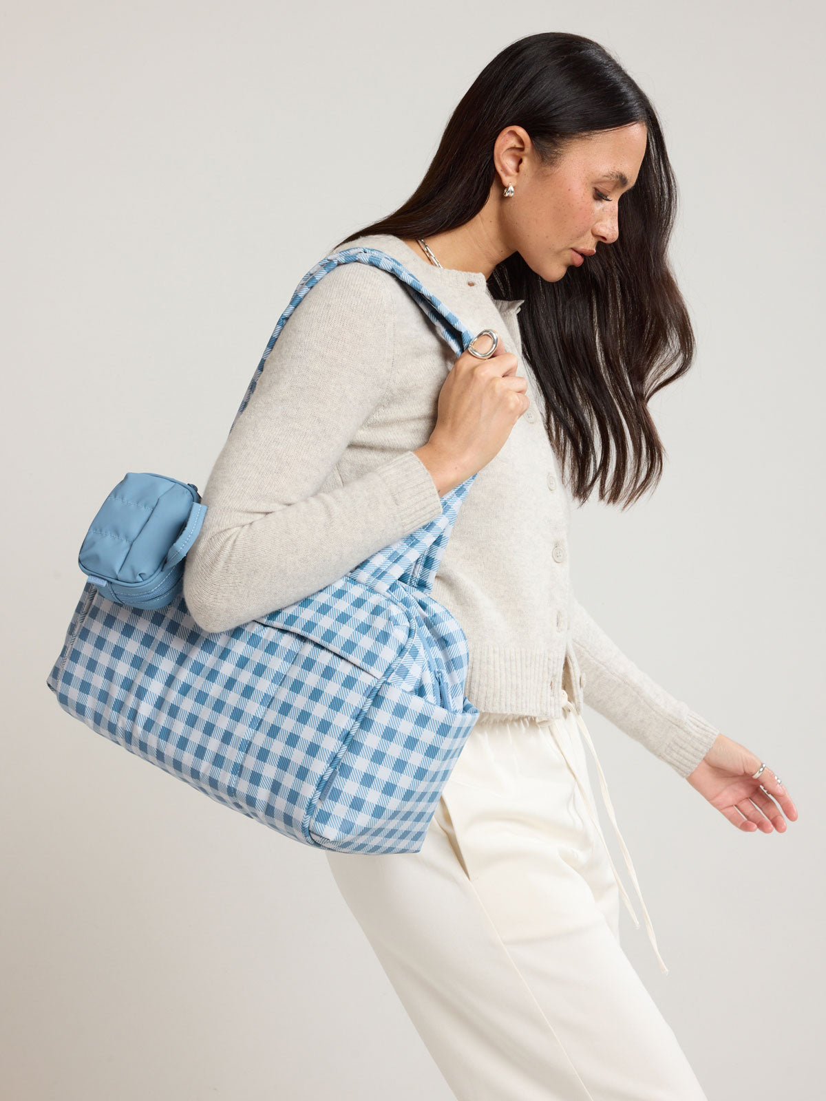 Woman wearing the CALPAK Luka Mini Duffel in white and blue gingham print in French Blue Gingham; DLM2501-FRENCH-BLUE-GINGHAM