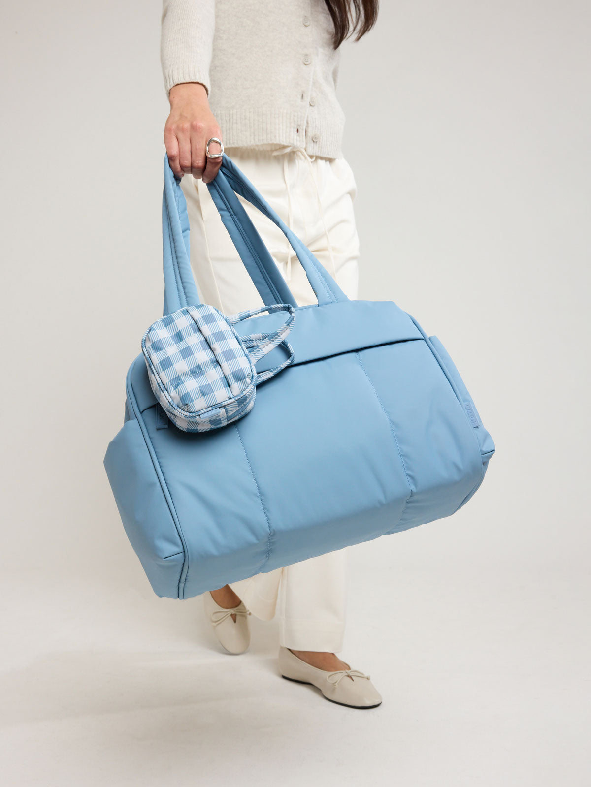 Model holding the CALPAK Luka Mini Duffel in light blue French Blue; DLM2501-FRENCH-BLUE