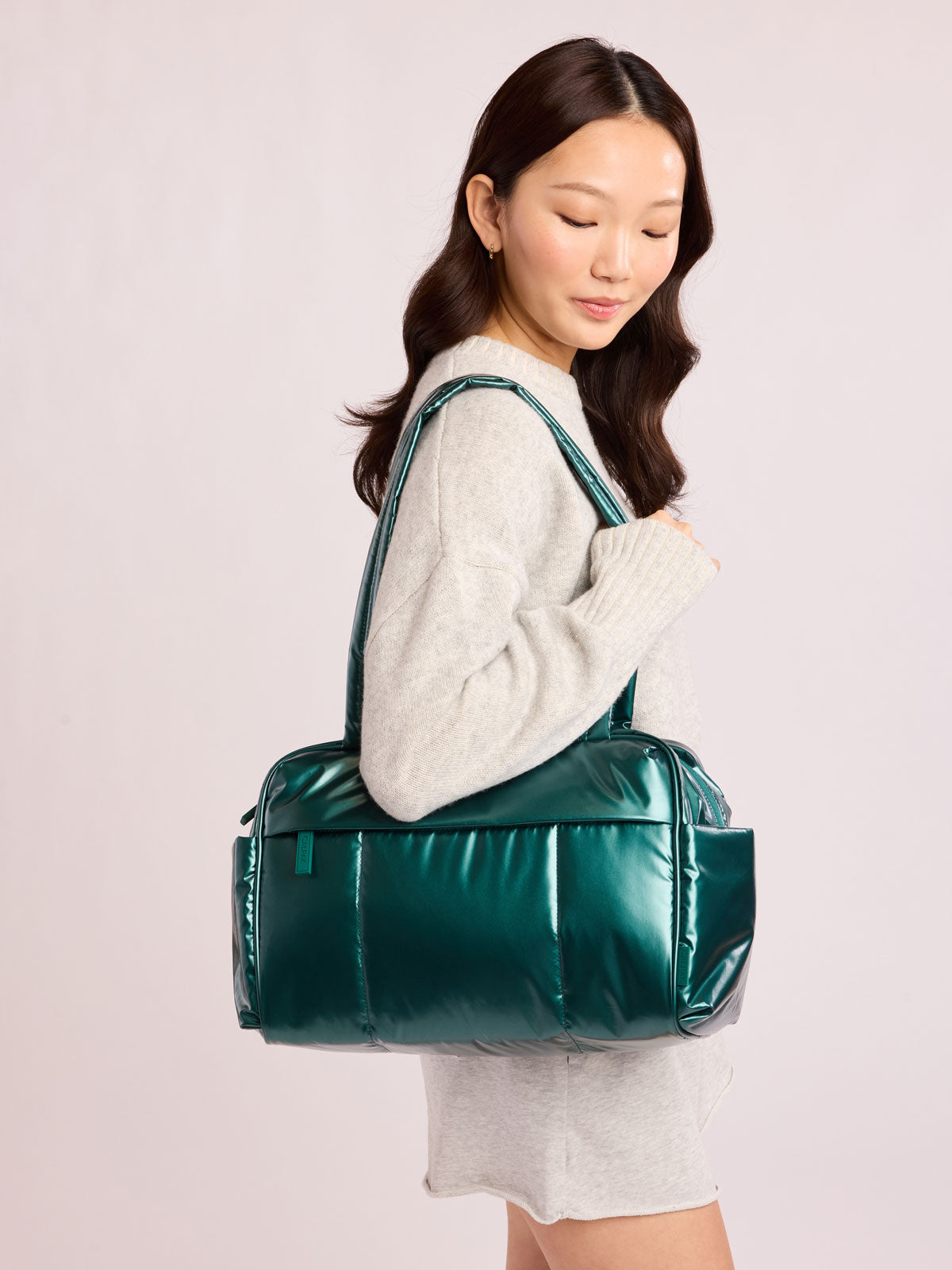 Woman wearing CALPAK Luka Mini Duffel in dark green shiny Glazed Kale; DLM2501-GLAZED-KALE