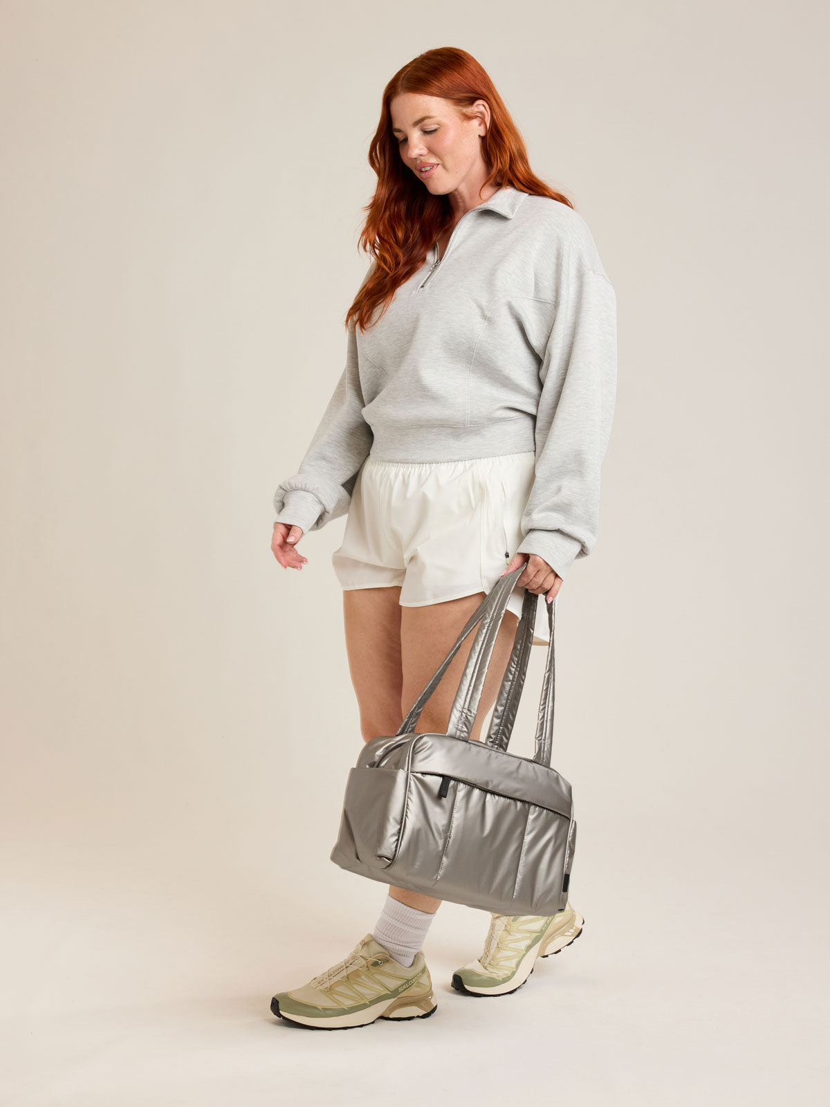Model holding CALPAK Luka Mini Duffel in metallic grey on a white background; DLM2501-GUNMETAL