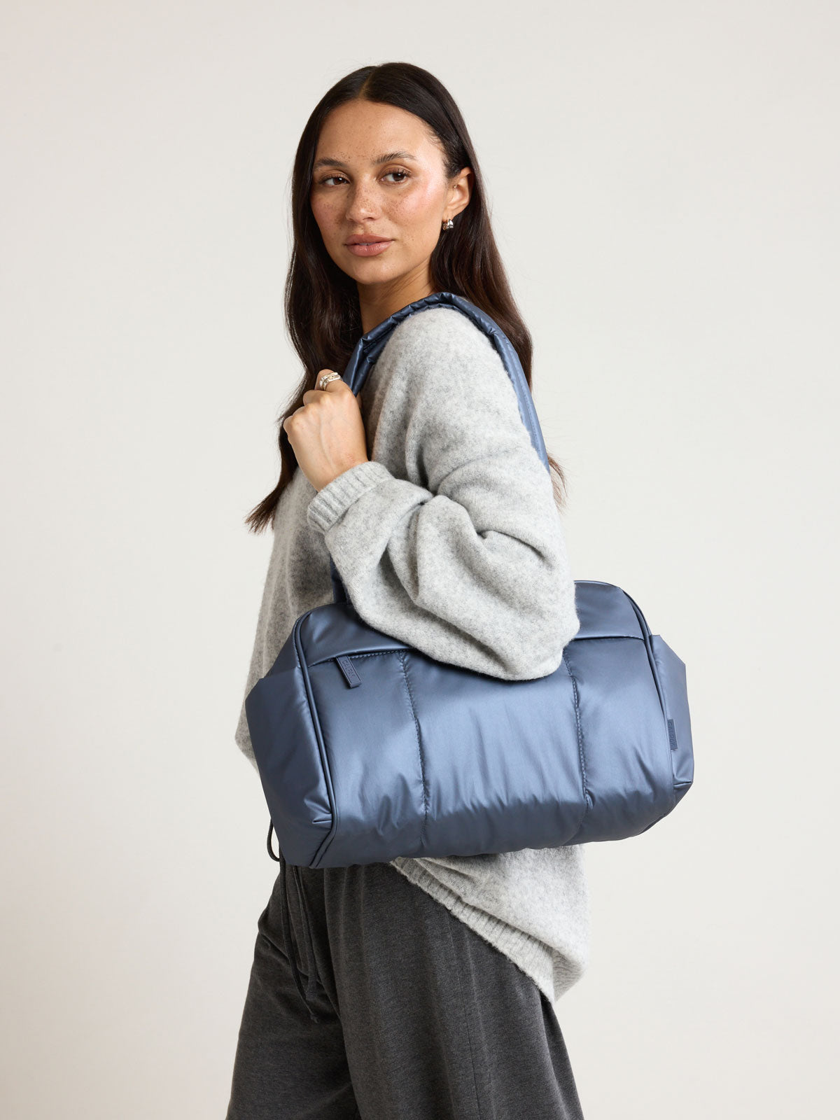 Model wearing the CALPAK Luka Mini Duffel in metallic dark blue Metallic Indigo; DLM2501-METALLIC-INDIGO