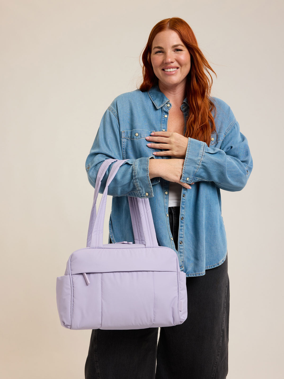 Model with CALPAK Luka Mini Duffel in light purple Orchid on a white background; DLM2501-ORCHID