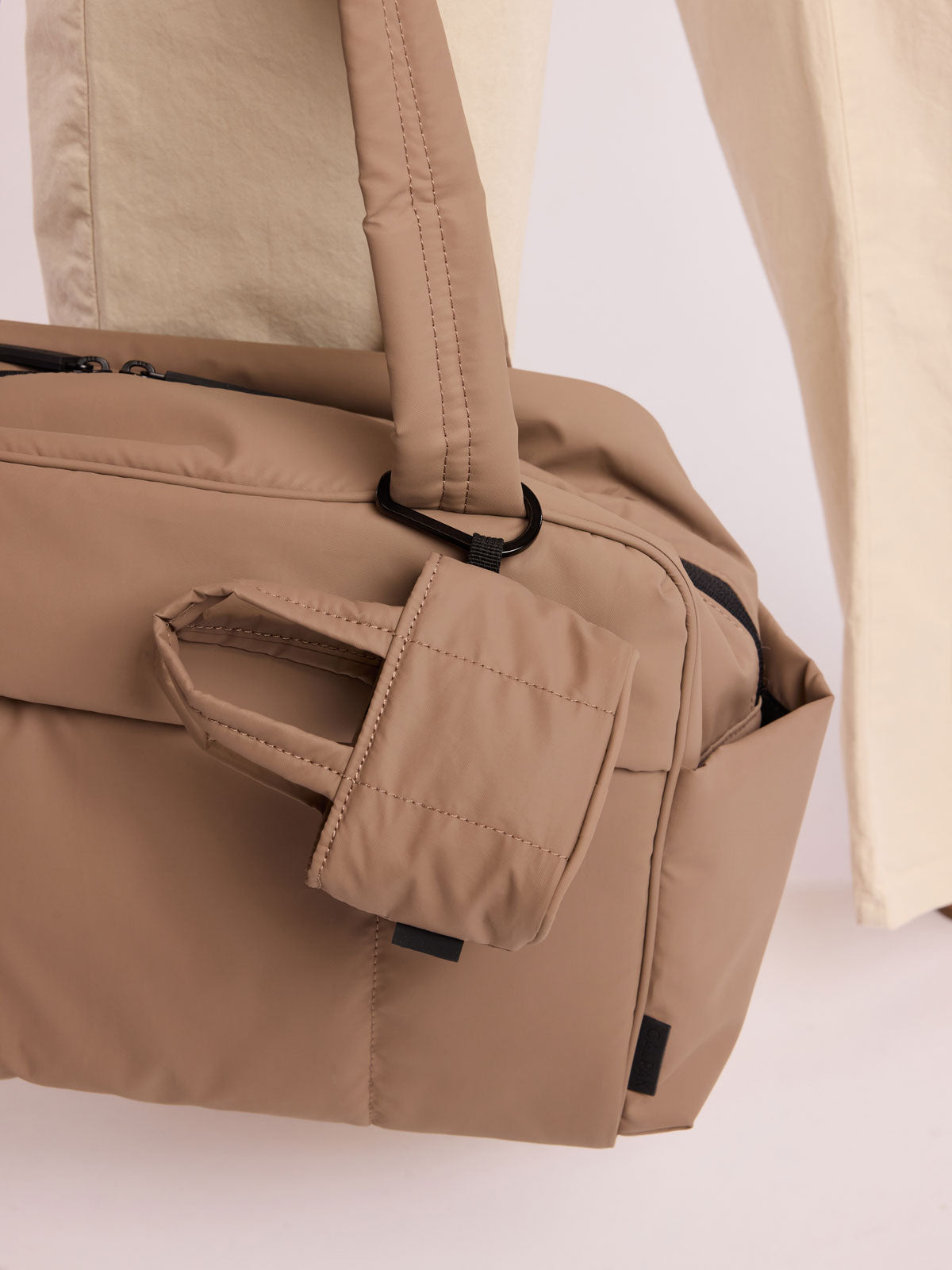 Model with CALPAK Luka Tote Zip Bag Charm in light brown Chocolate with carabiner attached on a bag; AMT2601-CHOCOLATE