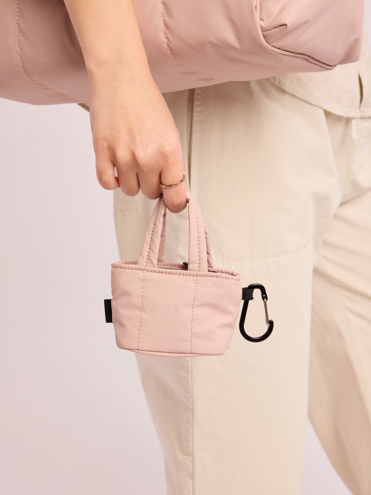 Model holding CALPAK Luka Tote Zip Bag Charm in light pink Rose Quartz  with carabiner; AMT2601-ROSE-QUARTZ