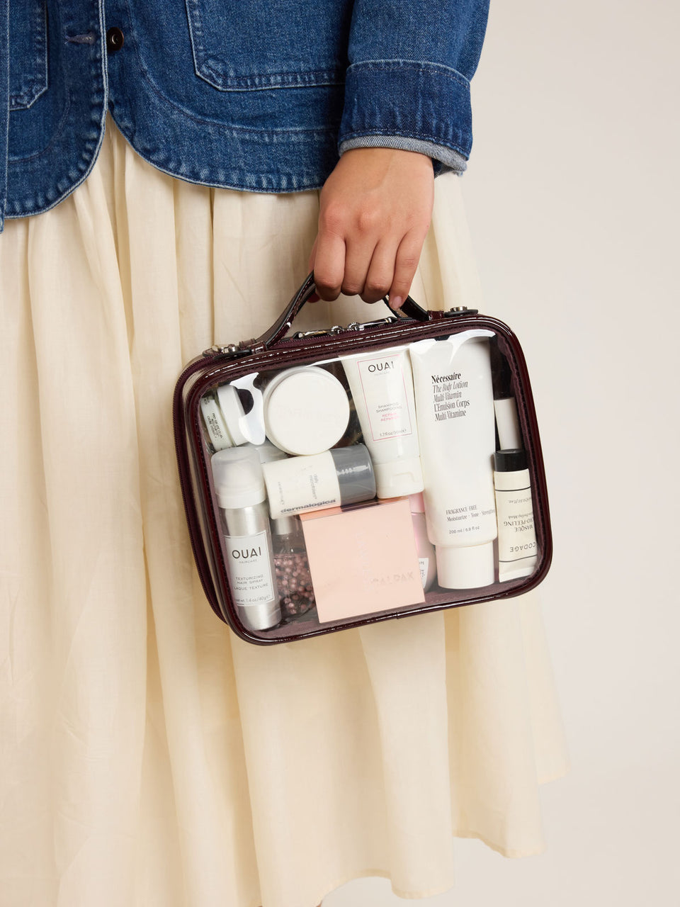 Model holding CALPAK Medium Clear Cosmetic Case in maroon Glazed Dark Cherry on a white background; CMM2201-GLAZED-DARK-CHERRY