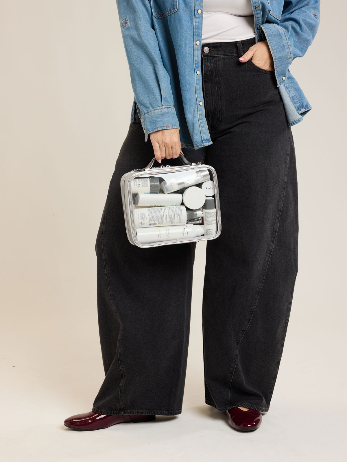 Model holding CALPAK Medium Clear Cosmetic Case in Silver on a white background; CMM2201-SILVER