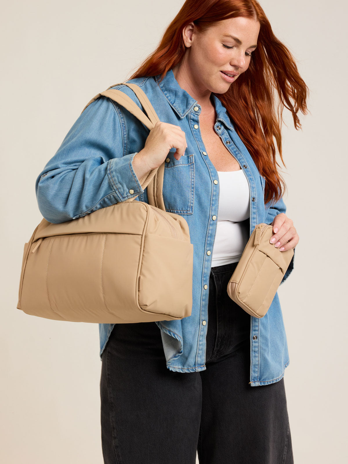 Model holding CALPAK Luka Zip Passport Wallet in beige Latte on a white background; PZW2301-LATTE