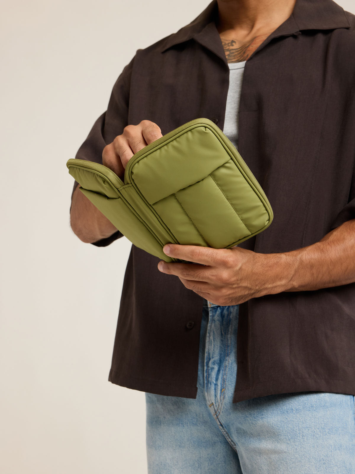 Model holding an opened CALPAK Luka Zip Passport Wallet in dark green Pistachio on a white background; PZW2301-PISTACHIO
