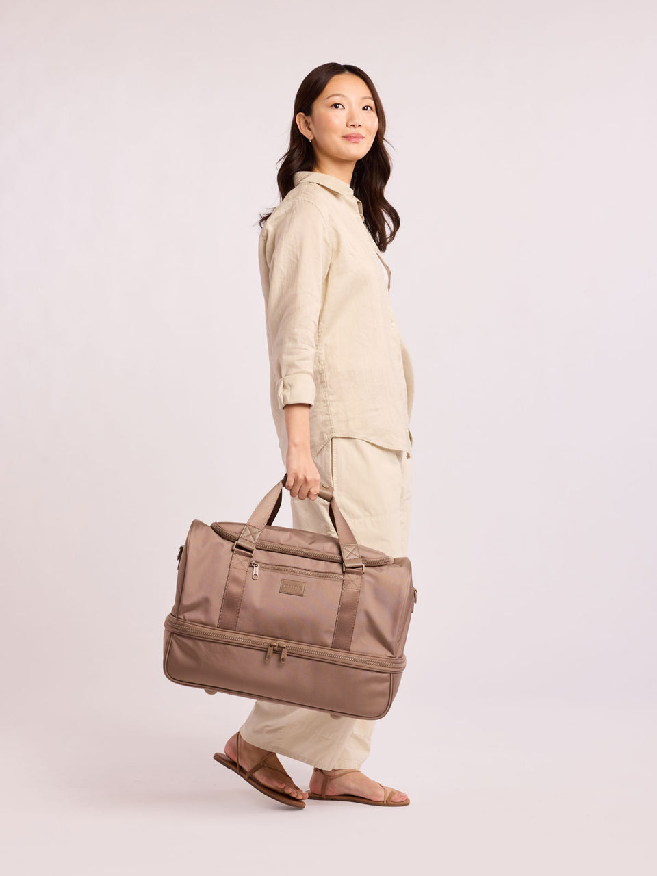 Woman with CALPAK Stevyn Duffel with Shoe Compartment in brown Chocolate; DST7019-CHOCOLATE