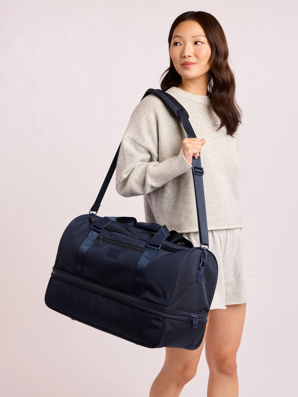 Woman with CALPAK Stevyn Duffel with Shoe Compartment in dark blue Navy; DST7019-NAVY