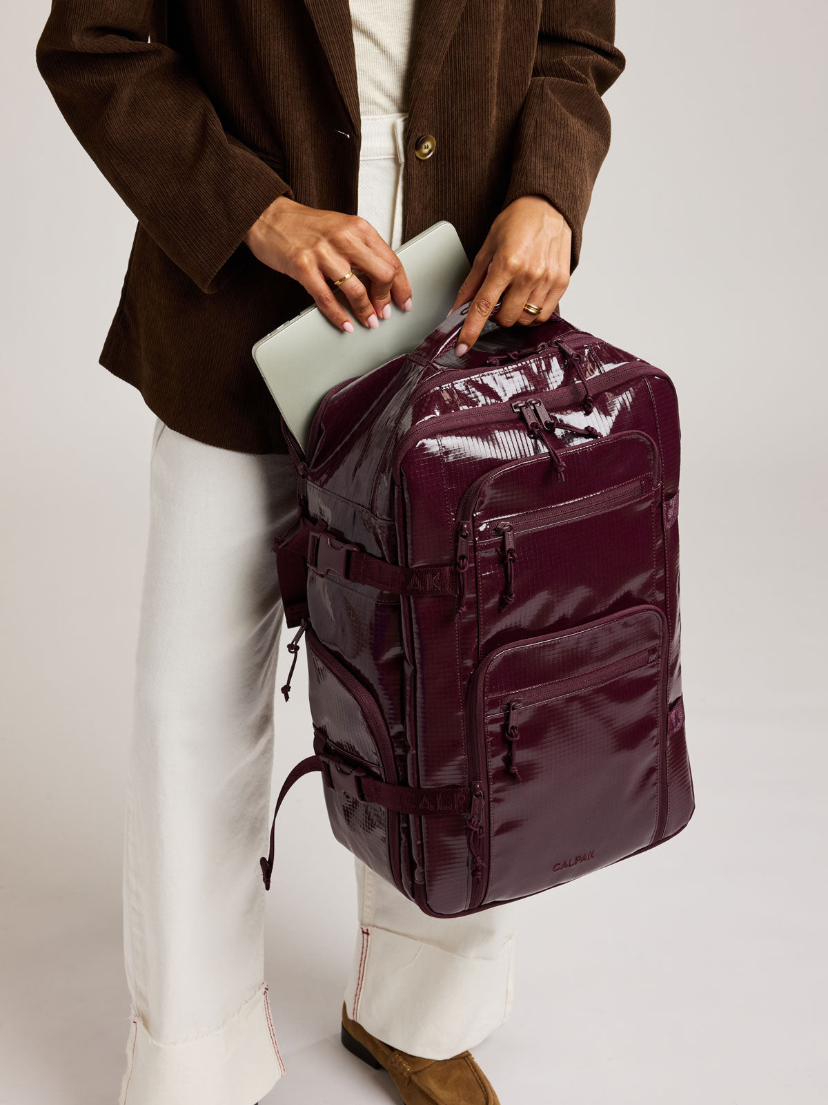 Person holding CALPAK Terra 26L Laptop Backpack in dark red Dark Cherry with multiple pockets on a white background; BPH2201-DARK-CHERRY