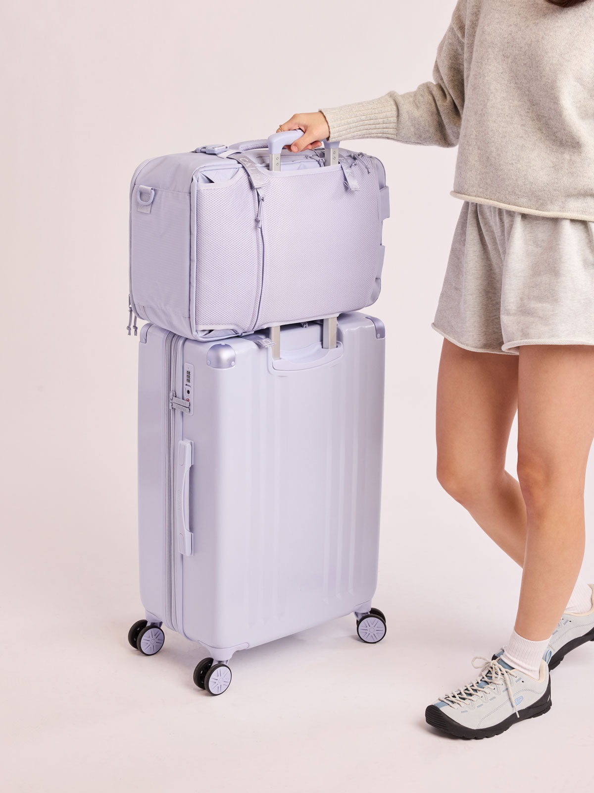 Model using luggage trolley sleeve of CALPAK Terra 26L Laptop Duffel Backpack with multiple pockets in light purple Sea Glass on a white background; BPH2201-SEA-GLASS