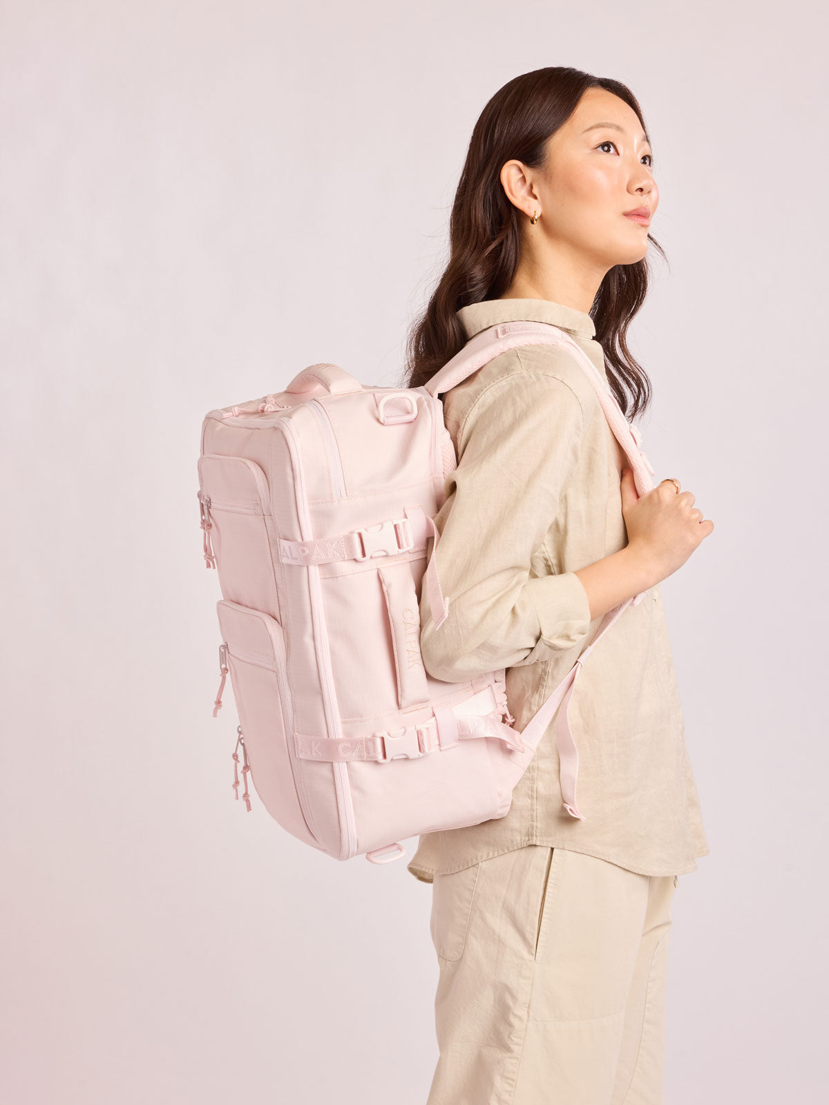 Model waring the CALPAK Terra 26L Laptop Duffel Backpack with multiple pockets in light pink Shell Pink on a white background; BPH2201-SHELL-PINK