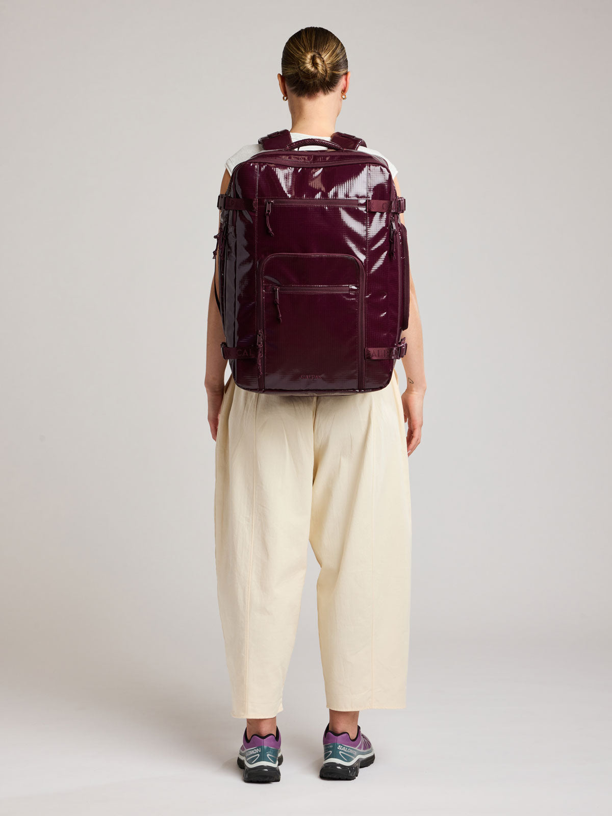 Woman wearing the CALPAK Terra 35L Laptop Backpack Duffel in dark red Dark Cherry with tan accents on a white background; BPTL2601-DARK-CHERRY