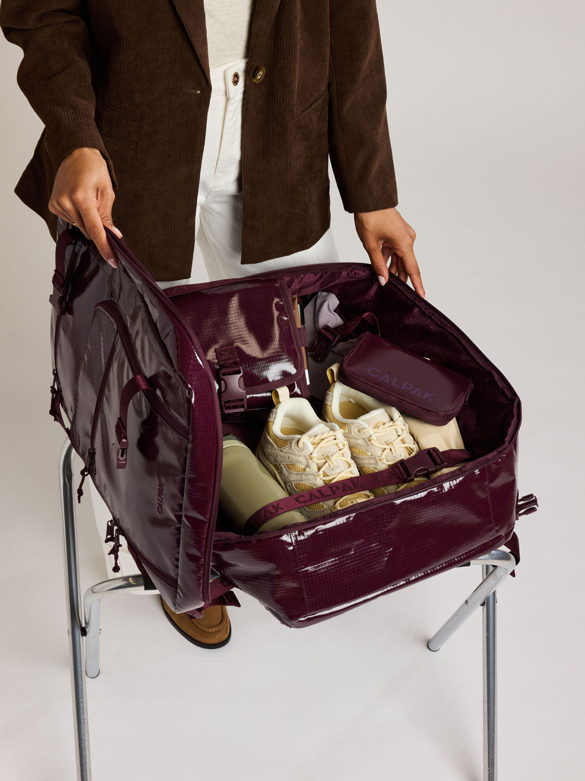 Woman packing shoes in the CALPAK Terra 35L Laptop Backpack Duffel in dark red Dark Cherry with tan accents on a white background; BPTL2601-DARK-CHERRY