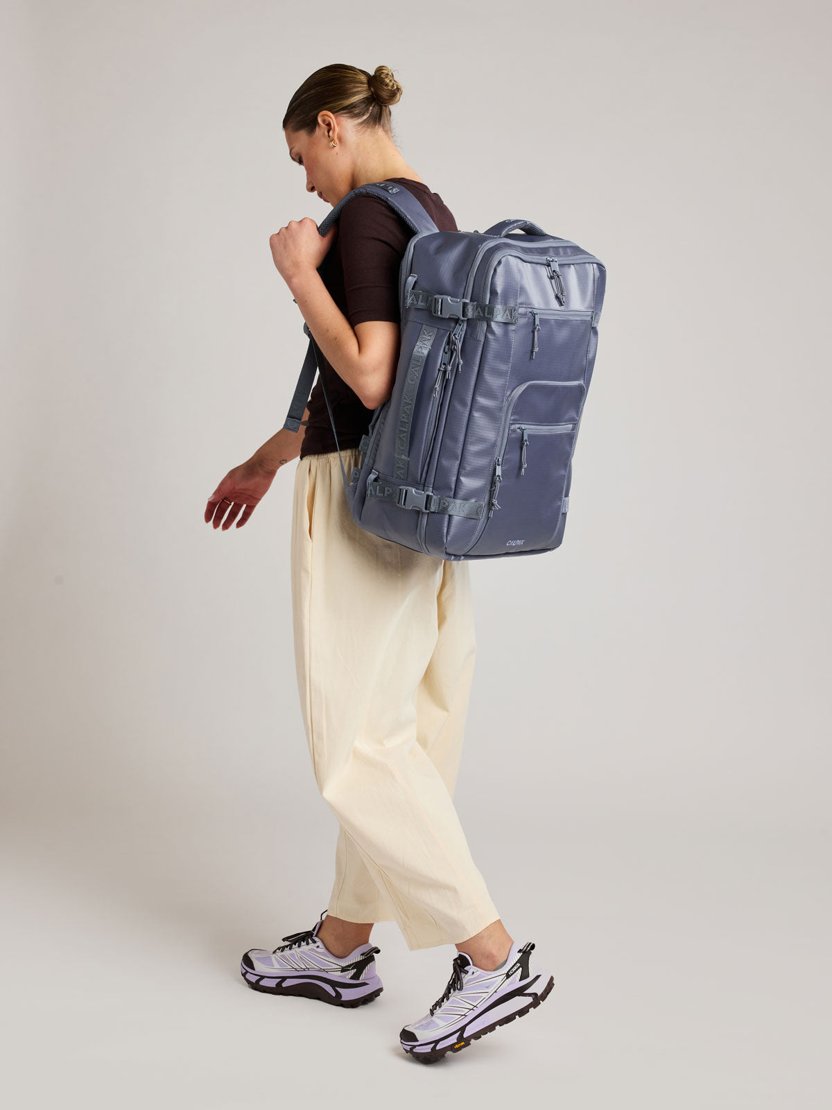 Woman wearing the CALPAK Terra 35L Laptop Backpack Duffel in matte dark blue Indigo with tan accents on a white background; BPTL2601-INDIGO