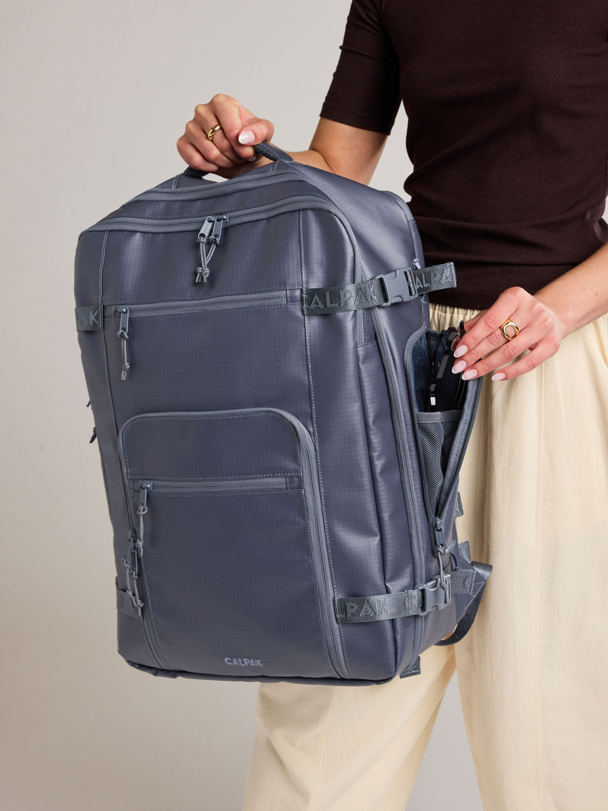 Woman holding the CALPAK Terra 35L Laptop Backpack Duffel in matte dark blue Indigo with tan accents on a white background; BPTL2601-INDIGO