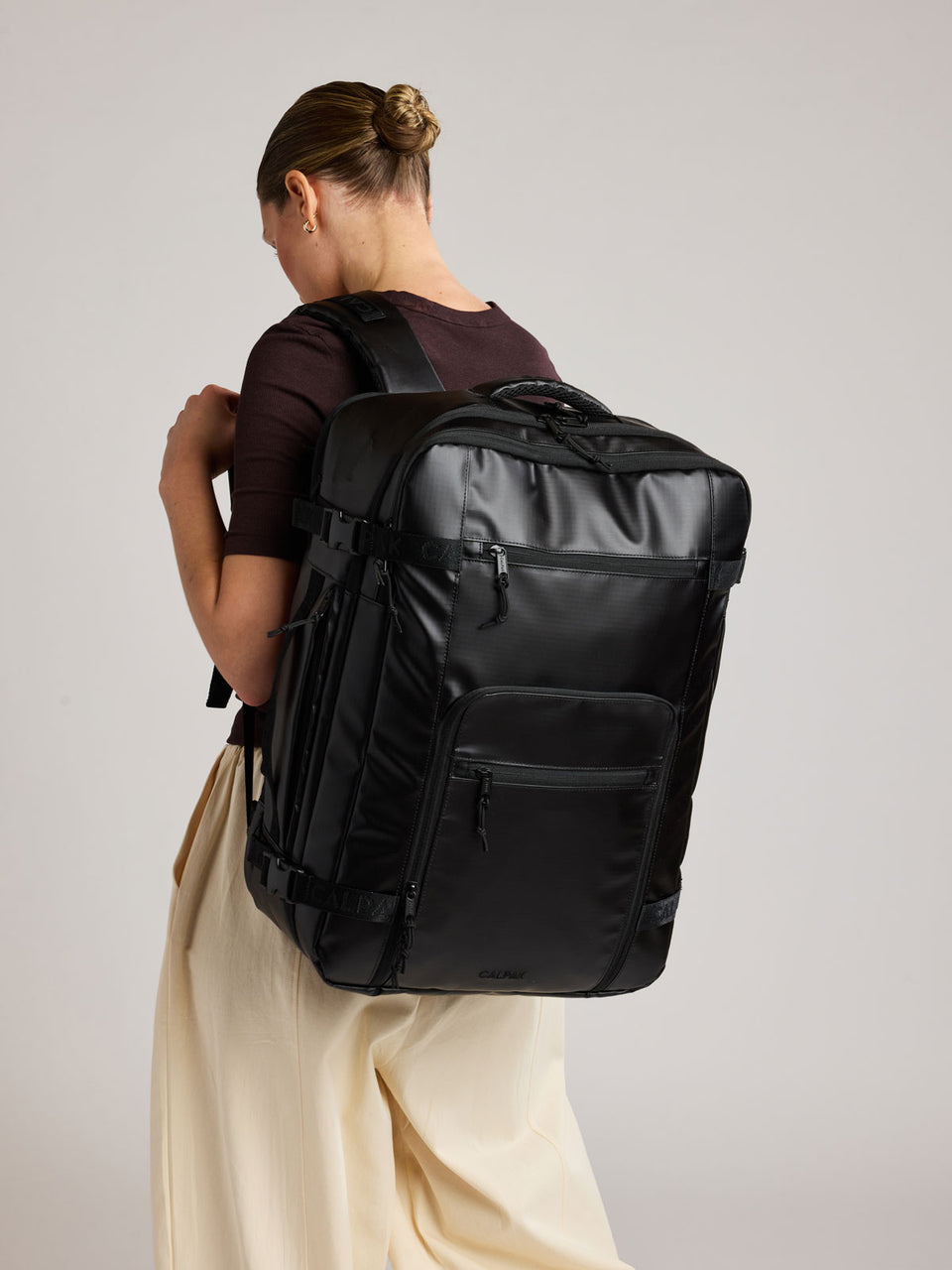 Woman wearing the CALPAK Terra 35L Laptop Backpack Duffel in matte black Obsidian on a white background;  BPTL2601-MATTE-OBSIDIAN