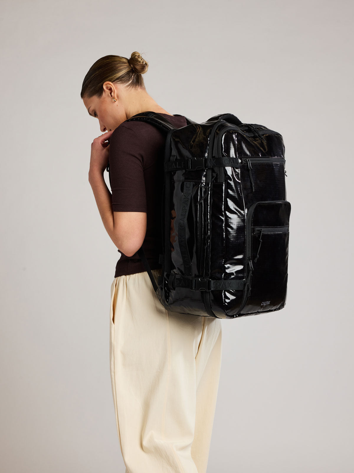 Woman wearing the CALPAK Terra 35L Laptop Duffel Backpack in shiny black Obsidian on a white background; BPTL2601-OBSIDIAN
