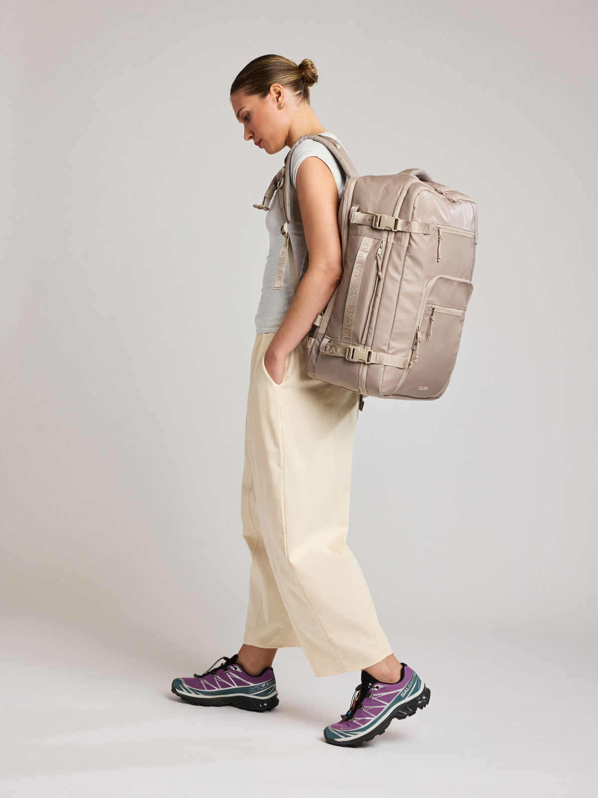 Woman wearing the CALPAK Terra 35L Laptop Backpack Duffel in beige Stone on a white background; BPTL2601-STONE