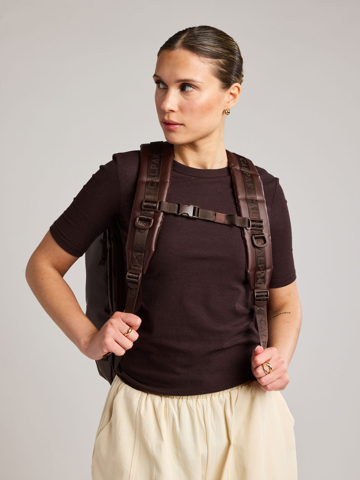 Woman wearing the CALPAK Terra 35L Laptop Backpack Duffel in matte brown Walnut on a white background; BPTL2601-WALNUT