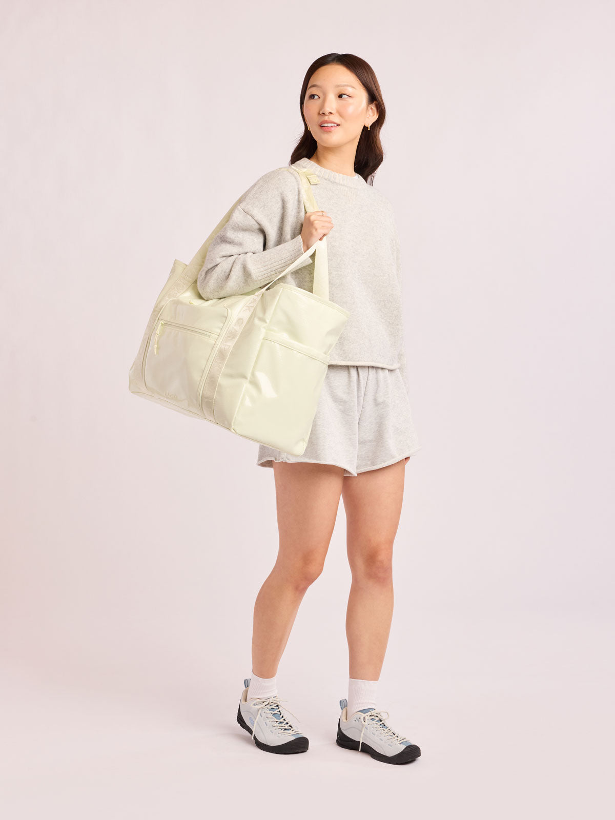 Model wearing beige with the CALPAK Terra 35L Tote Bag with multiple pockets and shoulder straps in shiny light green Celadon on a white background; TTO2401-CELADON