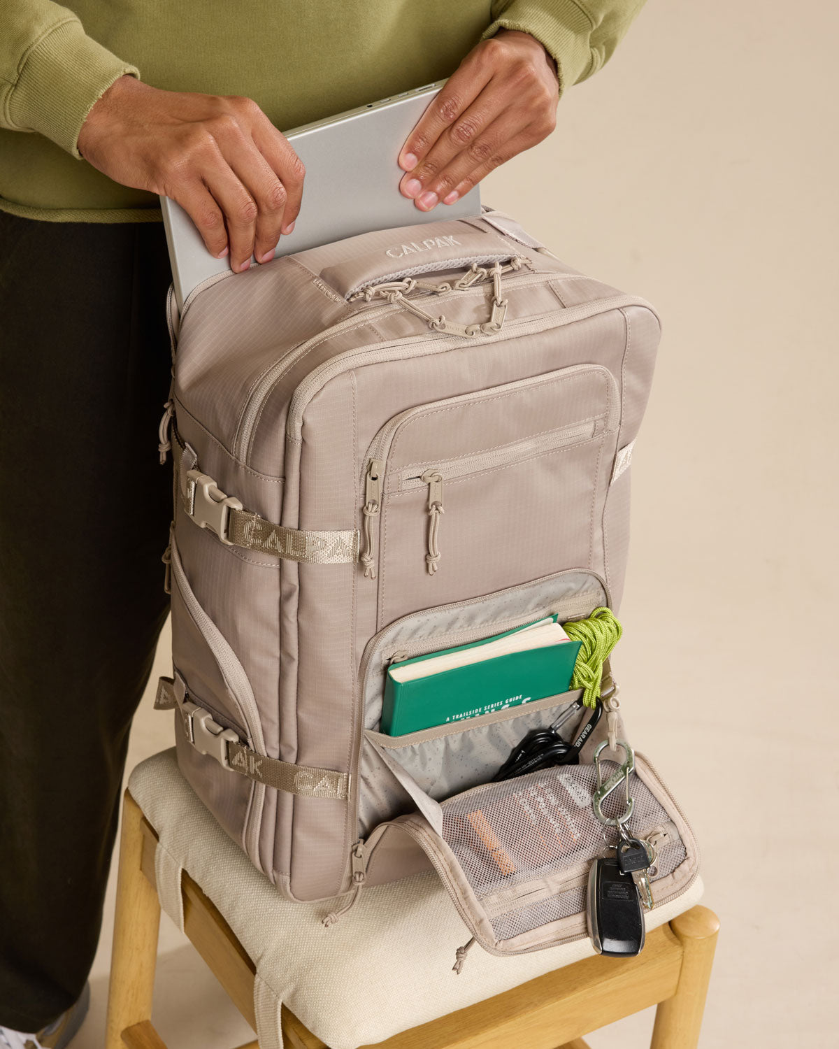 Model putting in laptop into CALPAK Terra 26L Laptop Duffel Backpack in beige Stone front view; BPH2201-STONE