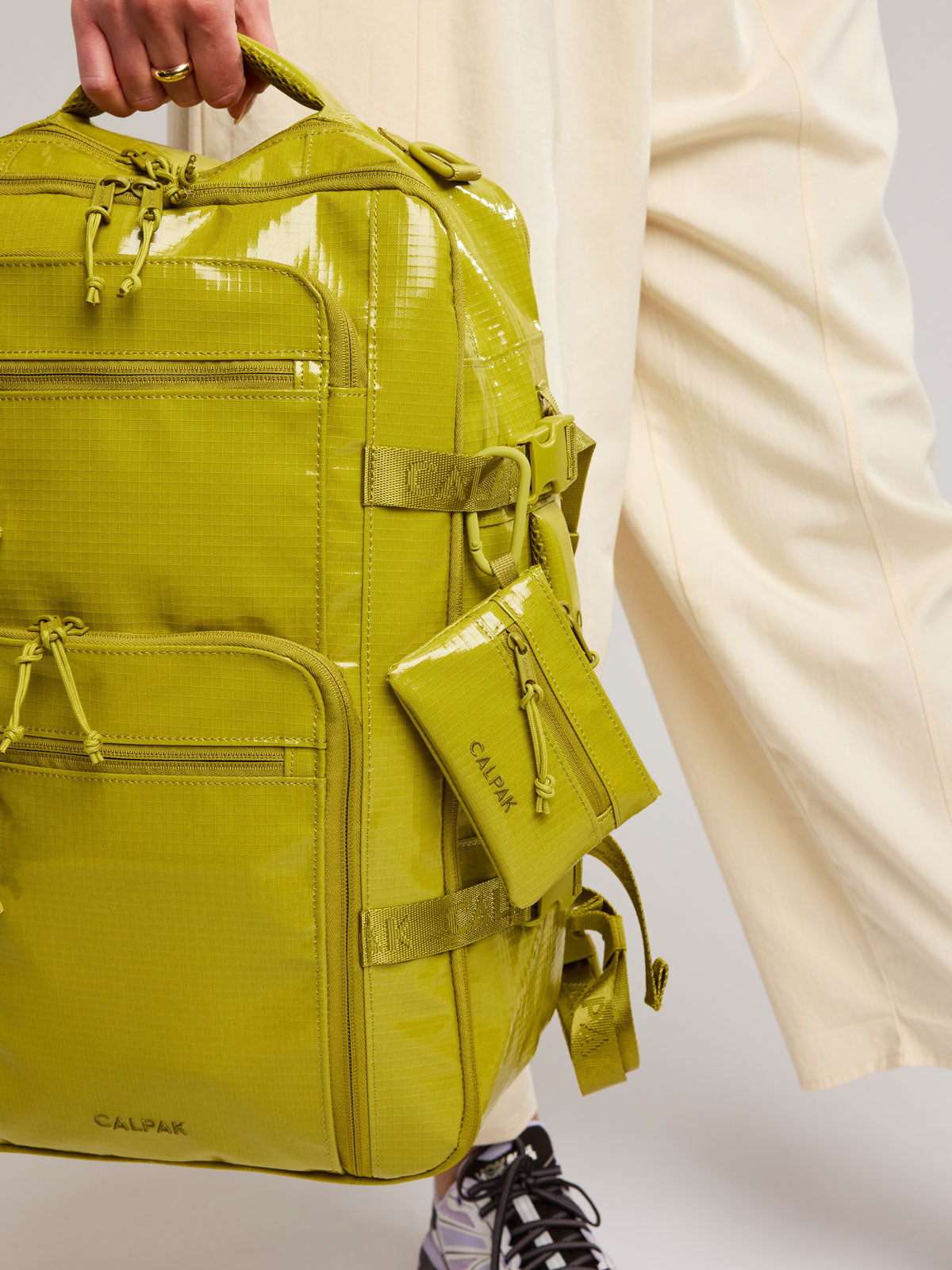 Yellow green Wasabi of CALPAK Terra Clippable Card Pouch with carabiner clip and zipper clipped on a backpack; TPC2401-WASABI