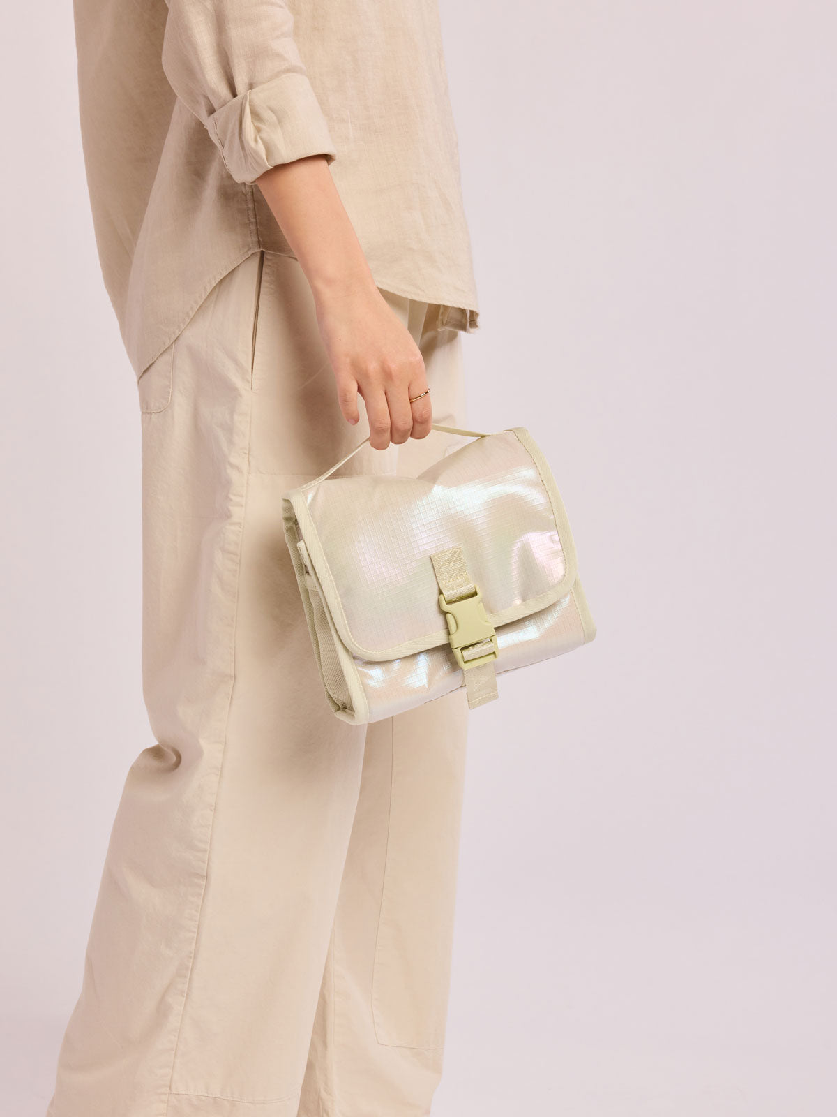 Model holding CALPAK Terra Hanging Toiletry Bag in shiny white Moonbeam with front buckle; THY2201-MOONBEAM