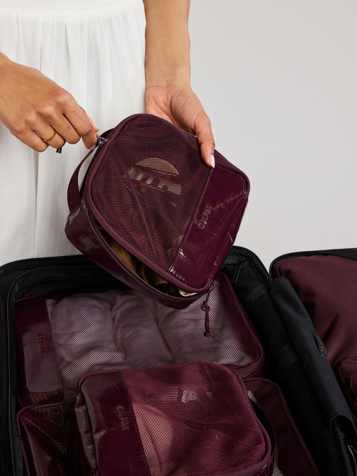 Person packing in a suitcase the CALPAK Terra 5pc Packing Cube Set in dark red Dark Cherry on a white background; PCT2601-DARK-CHERRY