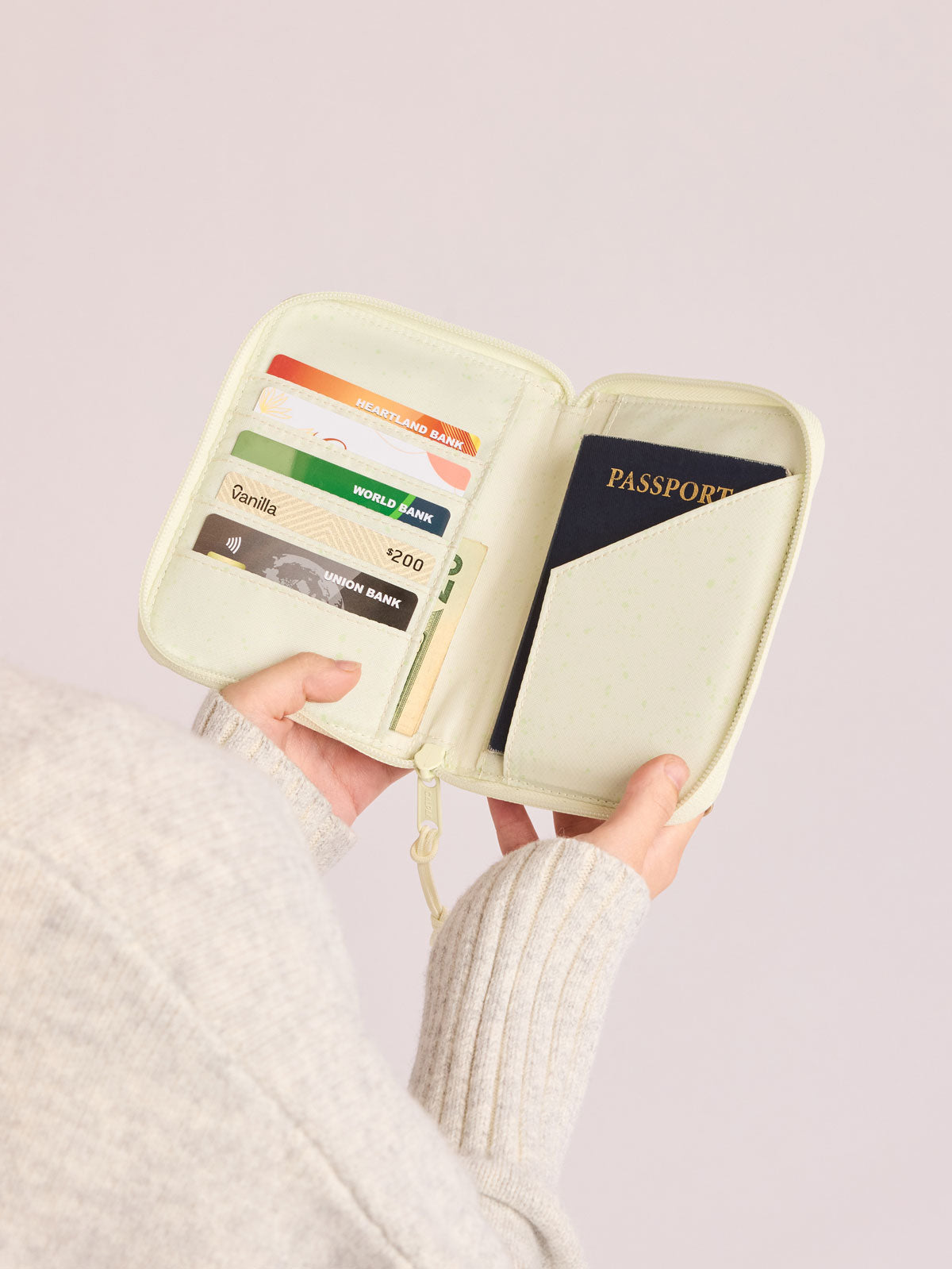Person holding open Front side of CALPAK Terra Zip Passport Wallet in light green Celadon; ATPW2501-CELADON