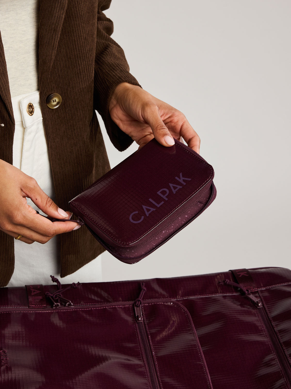 Person holding the  CALPAK Terra Zip Passport Wallet in dark red Dark Cherry on a white background; ATPW2501-DARK-CHERRY