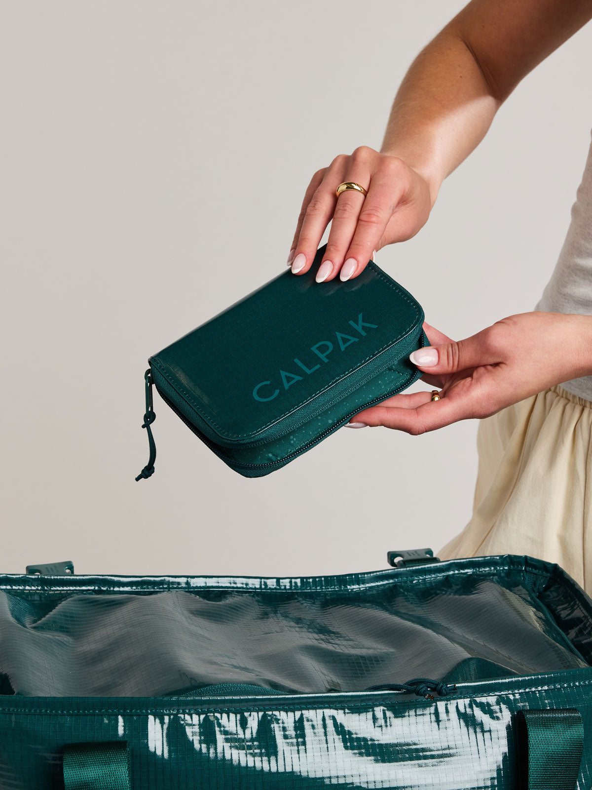 Model holding the CALPAK Terra Zip Passport Wallet in blue green Kale on a white background; ATPW2501-KALE