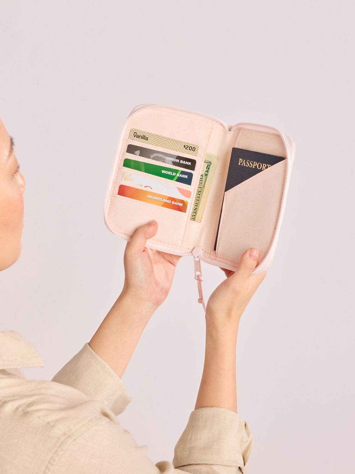 Model holding open the CALPAK Terra Zip Passport Wallet in light pink Shell Pink; ATPW2501-SHELL-PINK