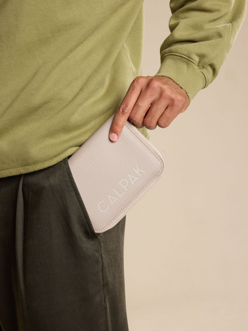Model with CALPAK Terra Zippered Passport Wallet in beige Stone front view; ATPW2501-STONE