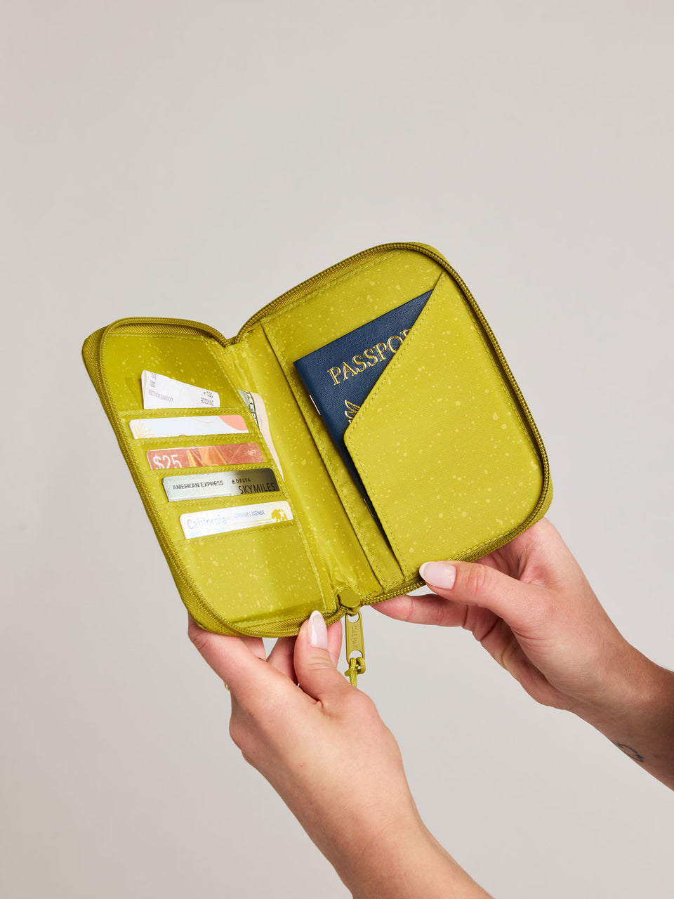 Person holding open a  CALPAK Terra Zip Passport Wallet in yellow green Wasabi with cards and a passport inside; ATPW2501-WASABI