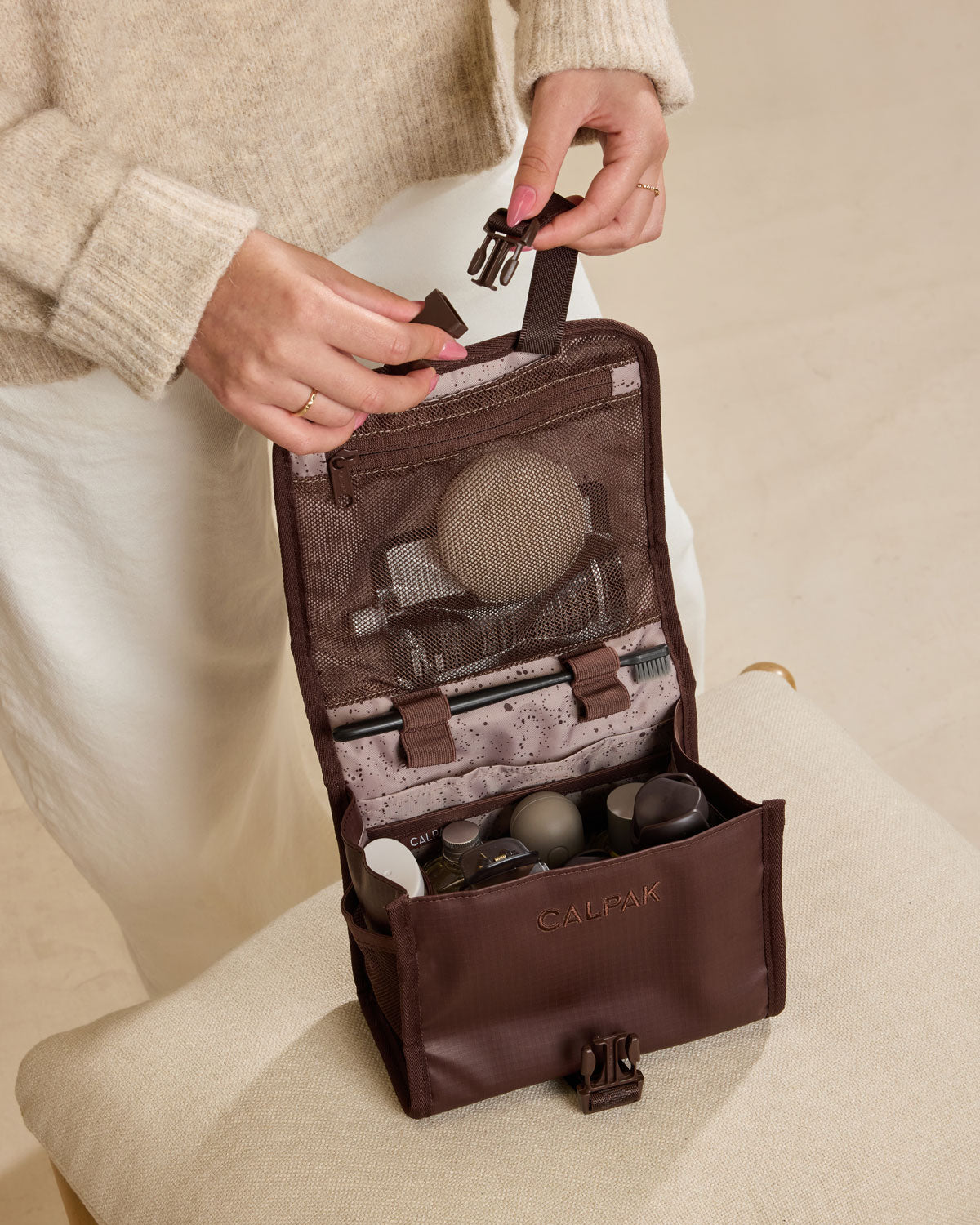 Model closing the CALPAK Terra Hanging Toiletry Bag in brown Walnut; THY2201-WALNUT