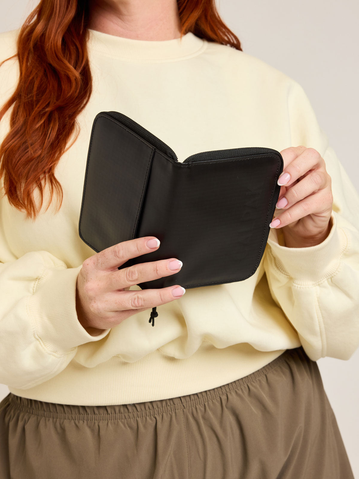 Model with CALPAK Terra Zippered Passport Wallet in black Matte Obsidian front view; ATPW2501-MATTE-OBSIDIAN