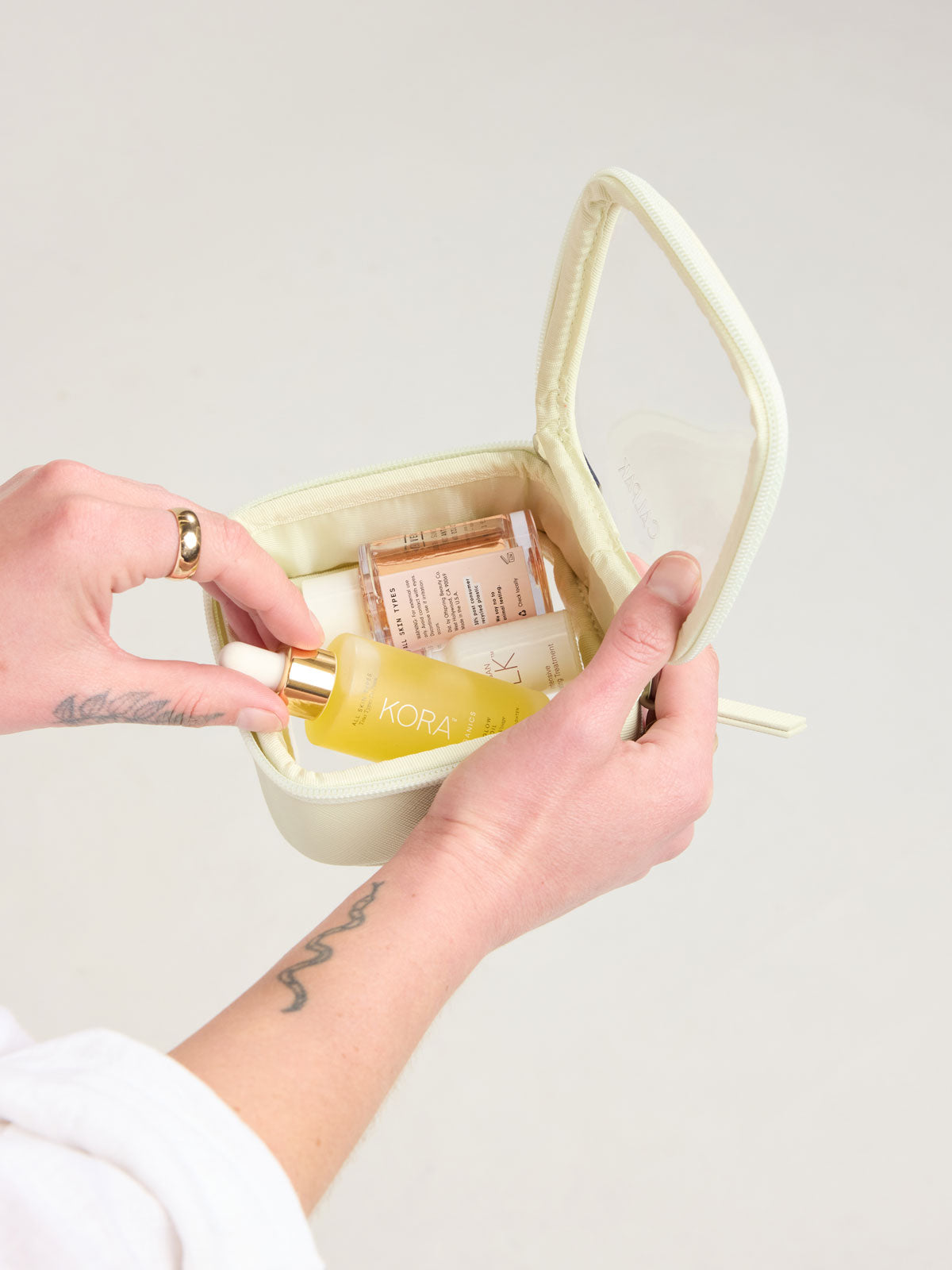 Person adding toiletry into CALPAK Tiny Clear Cosmetic Case in light green Celadon; CCT2501-CELADON