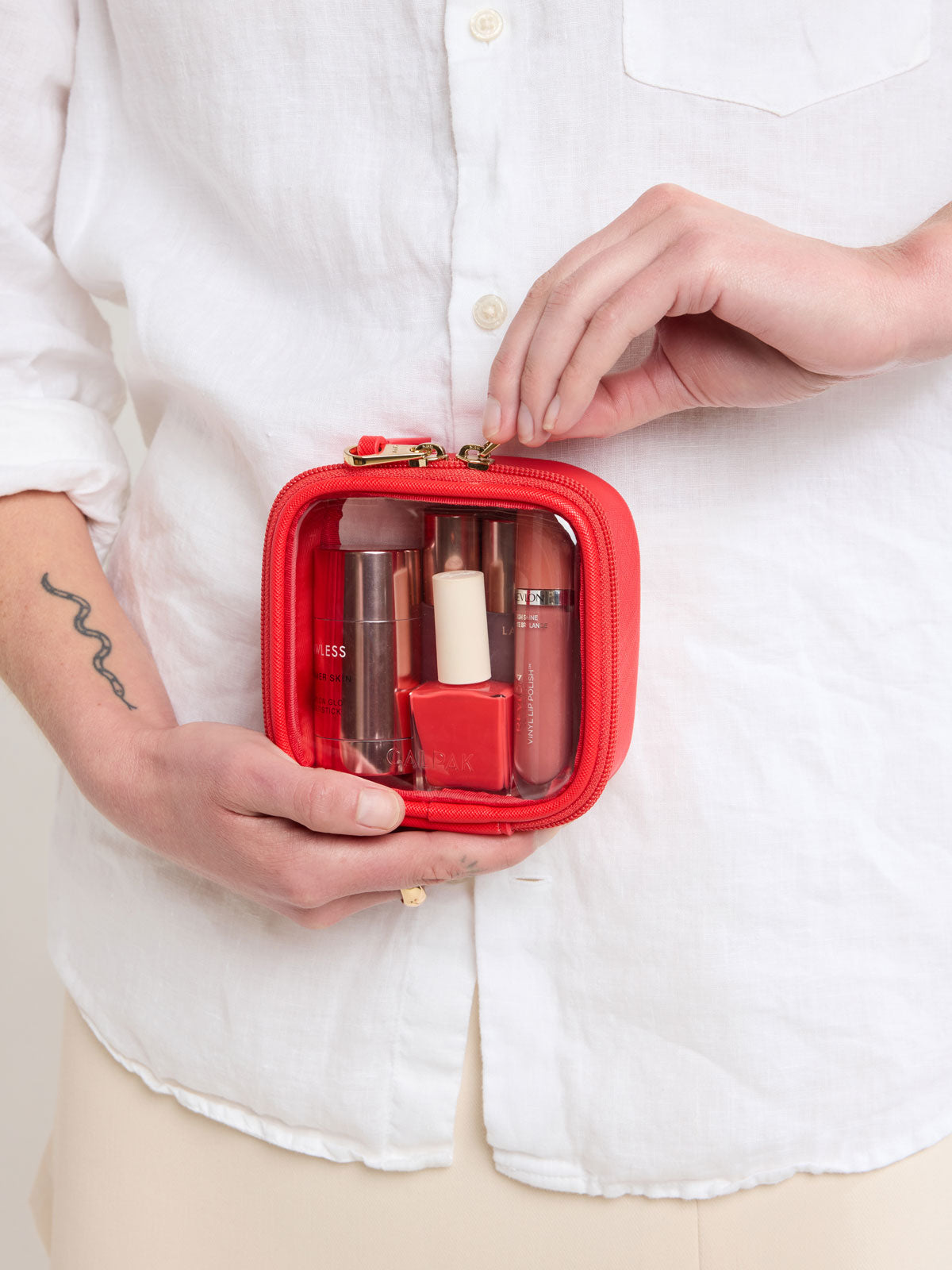 Person closing zipper of CALPAK Tiny Clear Cosmetic Case in red Tomato; CCT2501-TOMATO
