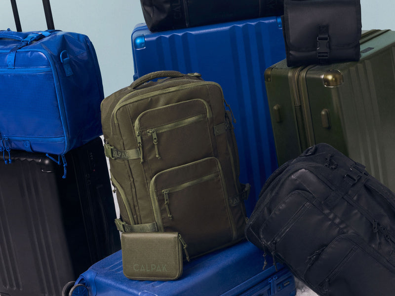 Green, blue and black backpacks with visible brand logo on a pile of suitcases and bags from CALPAK